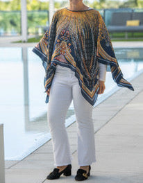 Woman wearing a patterned poncho and white pants standing by a pool.