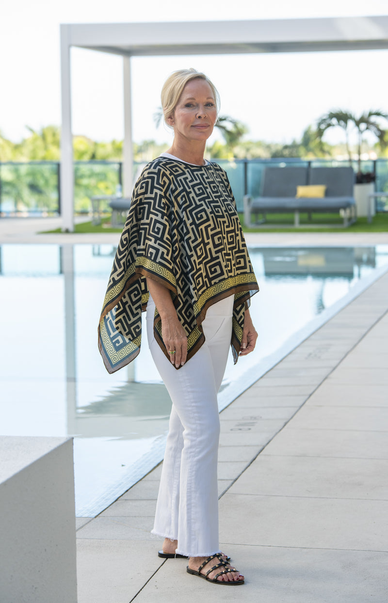 Woman wearing a patterned shawl and white pants by a poolside.